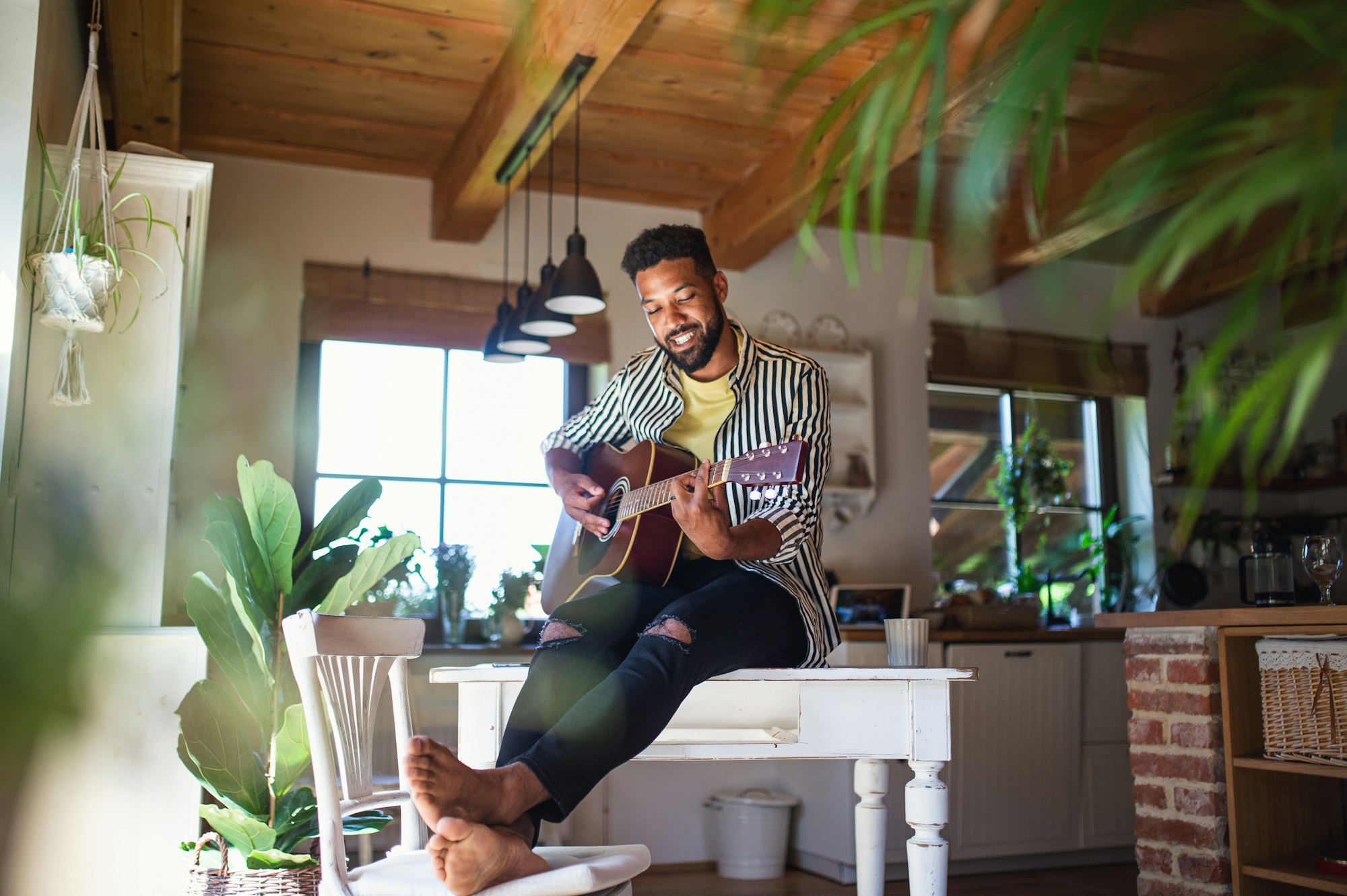 Happy young man with guitar indoors at home, relaxing